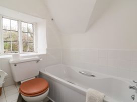 A bathroom with a toilet with a wooden seat a bathtub with a towel on the edge and a window at Dragon House in Bilbrook near Minehead