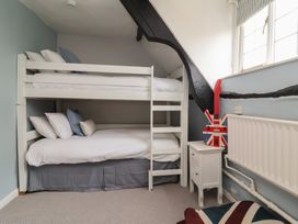 A bedroom with a white bunk bed pillows a bedside table with a guitar and a radiator at Dragon House in Bilbrook near Minehead