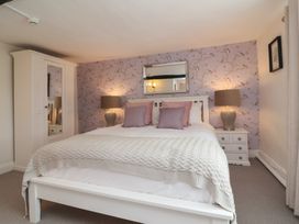 A bedroom with a white bed frame and knitted blanket two bedside tables with lamps and a wardrobe at Dragon House in Bilbrook near Minehead