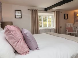 A bedroom with a bed featuring pink and purple pillows a window with curtains and a white chair with a pink cushion at Dragon House in Bilbrook near Minehead