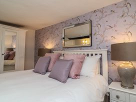 A bedroom with a white bed frame pink and purple pillows bedside tables with lamps a wardrobe with mirrored doors and bird patterned wallpaper at Dragon House in Bilbrook near Minehead