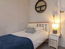 A bedroom with a white bed and blue blanket beside a white nightstand with lamp at Dragon House in Bilbrook near Minehead