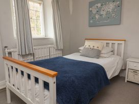 A bedroom with a white bed with blue blanket and pillows next to a window with striped curtains at Dragon House in Bilbrook near Minehead