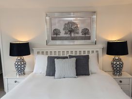 A bedroom with a bed framed by two side tables each with a lamp and a tree picture on the wall at Dragon House in Bilbrook near Minehead