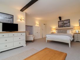 A bedroom with a bed between two lamps and nightstands a dresser with a television and an armchair at Dragon House in Bilbrook near Minehead
