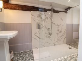 A bathroom with a walk-in shower featuring marble wall tiles a pedestal sink patterned floor tiles and exposed wooden beams at Dragon House in Bilbrook near Minehead