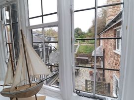 A view of a stone wall house and patio with wooden outdoor furniture seen through a window with a model sailboat on the windowsill at Dragon House in Bilbrook near Minehead