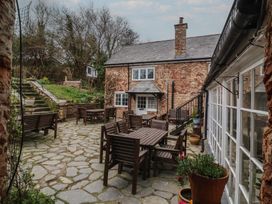 An outdoor patio with wooden tables and chairs stone paving and a stone house with a chimney at Dragon House in Bilbrook near Minehead
