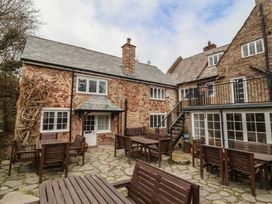 An outdoor patio area with wooden tables and benches in front of stone buildings with slate roofs at Dragon House in Bilbrook near Minehead