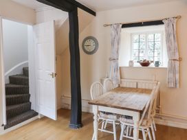 A dining area with a wooden table and four white chairs near a window with curtains and a clock on the wall at Dragon House in Bilbrook near Minehead