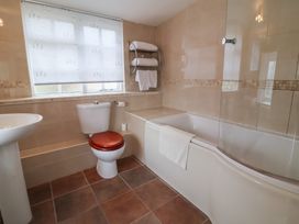 A bathroom with a toilet wooden seat a sink bathtub with towel and tiled walls and floor at Dragon House in Bilbrook near Minehead