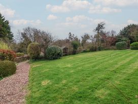 A garden with a gravel path surrounded by bushes and trees at Dragon House in Bilbrook near Minehead