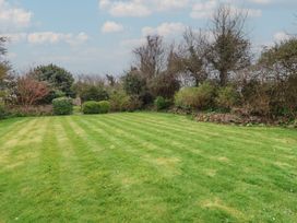 A large grassy lawn bordered by various bushes and trees under a partly cloudy sky