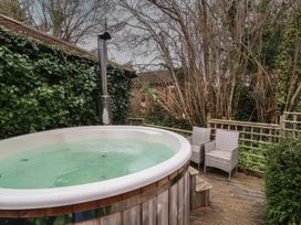 An outdoor hot tub on a wooden deck with two wicker chairs surrounded by trees and ivy at Gatekeeper's Cottage in Bilbrook near Minehead