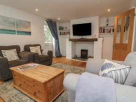 A living room with chairs a wooden coffee table a fireplace with a television and bookshelves at Gatekeeper's Cottage in Bilbrook near Minehead