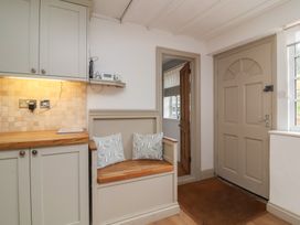 An entryway with a wooden door a bench with cushions and kitchen cabinets at Gatekeeper's Cottage in Bilbrook near Minehead