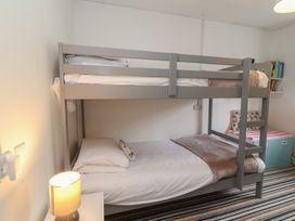 A bedroom with a gray bunk bed a small nightstand with a lit lamp a striped carpet and a storage bench with books on a wall shelf at Gatekeepers Cottage in Bilbrook near Minehead