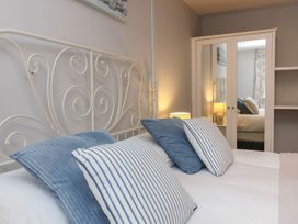 A bedroom with a white metal bed frame blue and white striped pillows a bedside lamp and a white mirrored wardrobe at Gatekeeper's Cottage in Bilbrook near Minehead