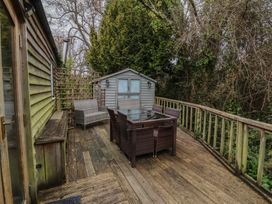 An outdoor wooden deck with a glass table and wicker chairs next to a wooden shed surrounded by trees at Gatekeeper's Cottage in Bilbrook near Minehead
