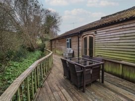 A wooden deck with a glass table and six chairs next to a wooden house with trees in the background at Gatekeeper's Cottage in Bilbrook near Minehead