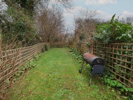 A narrow garden with grass lawn fenced on both sides and a barbecue grill at Gatekeeper's Cottage in Bilbrook near Minehead