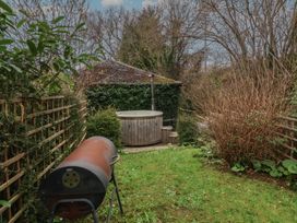 A garden with a rusty barbecue grill wooden hot tub and a shed covered in ivy at Gatekeeper's Cottage Bilbrook near Minehead