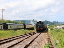 A steam locomotive pulling passenger cars on train tracks with green hills and signal posts in the background at Gatekeeper's Cottage in Bilbrook near Minehead