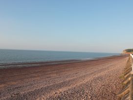 A pebble beach with calm sea and clear sky near a coastline with cliffs at Gatekeeper's Cottage in Bilbrook near Minehead