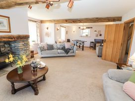 A living room with sofas a wooden coffee table flowers a stone fireplace and a foosball table at High Wood Foot in Bampton Cumbria