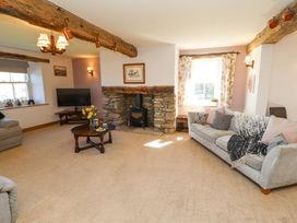 A living room with a stone fireplace a wood stove two sofas a television and wooden beams at High Wood Foot in Bampton Cumbria