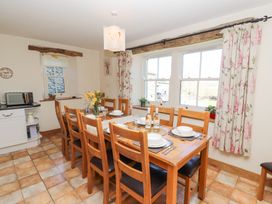A dining room with a wooden table set for eight with plates and wine bottles by windows with floral curtains at High Wood Foot in Bampton Cumbria