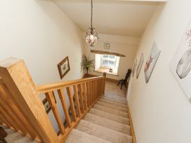 A carpeted staircase with wooden railing leading down to a window seat with a chair near the window at High Wood Foot in Bampton Cumbria