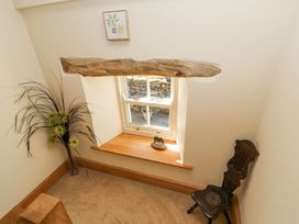 A small corner with a window and wooden sill a carved wooden chair a tall plant in a vase and a framed picture on the wall at High Wood Foot in Bampton Cumbria