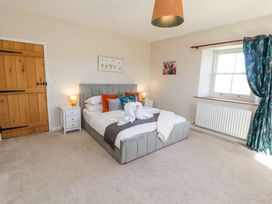 A bedroom with a double bed two bedside tables with lamps a wooden door and a window with blue curtains at High Wood Foot in Bampton Cumbria