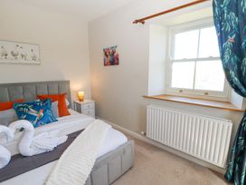 A bedroom with a bed with colorful pillows a nightstand with a lamp window with floral curtains and framed animal pictures on the wall at High Wood Foot in Bampton Cumbria