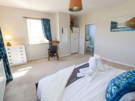 A bedroom with a bed featuring folded towel animals and pillows a wooden chair near a window with blue curtains a white chest of drawers and an en suite bathroom at High Wood Foot in Bampton Cumbria