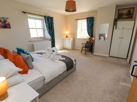 A bedroom with a bed with colorful pillows a wooden chair a dresser a wardrobe and two windows with curtains at High Wood Foot in Bampton Cumbria