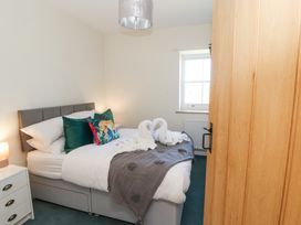 A bedroom with a bed with green and animal print pillows a towel swans decoration a bedside table with a lamp and a window at High Wood Foot in Bampton Cumbria