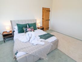 A bedroom with a bed with green pillows and a beige throw on a light green carpet at High Wood Foot in Bampton Cumbria