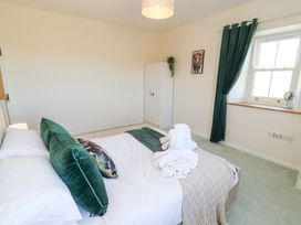 A bedroom with a bed with green pillows and white towels on top a white wardrobe a window with green curtains and a painting of a lion on the wall at High Wood Foot in Bampton Cumbria