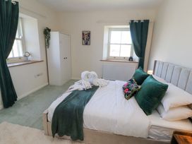 A bedroom with a bed with green pillows and blanket two windows with green curtains a white wardrobe and a wall painting at High Wood Foot in Bampton Cumbria