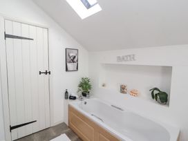 A bathroom with a bathtub a skylight a white door a plant and wall art at High Wood Foot in Bampton Cumbria