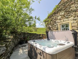 A hot tub next to a stone wall and plants at High Wood Foot in Bampton, Cumbria