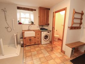A bathroom with shower, sink, washing machine, and toilet at High Wood Foot in Bampton, Cumbria