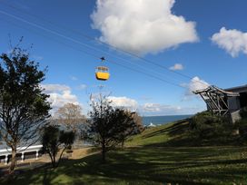 A yellow cable car suspended on wires above a grassy area with trees near the sea at 21 Taliesin Street in Llandudno
