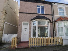 A terrace house with a bay window and white door behind a wooden fence at 21 Taliesin Street in Llandudno