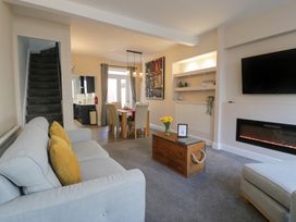 A living room with a sofa, coffee table with flowers, wall-mounted tv, electric fireplace, and dining area with table and chairs at 21 Taliesin Street in Llandudno