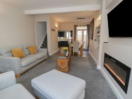 A living room with a gray sofa and yellow cushions a wooden chest as a coffee table a dining area with a table and chairs and a wall-mounted electric fireplace at 21 Taliesin Street in Llandudno