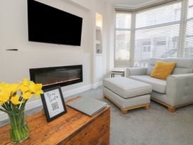 A living room with a couch, an ottoman, a wooden table with a vase of yellow flowers, a framed sign, an electric fireplace, and a wall-mounted TV at 21 Taliesin Street in Llandudno