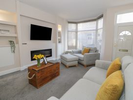 A living room with grey sofas yellow cushions a wooden chest used as a coffee table and a wall mounted television at 21 Taliesin Street in Llandudno